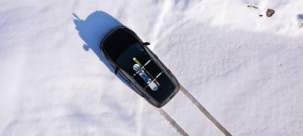 Black car with snowboard on roof driving through snow. Bird's eye perspective