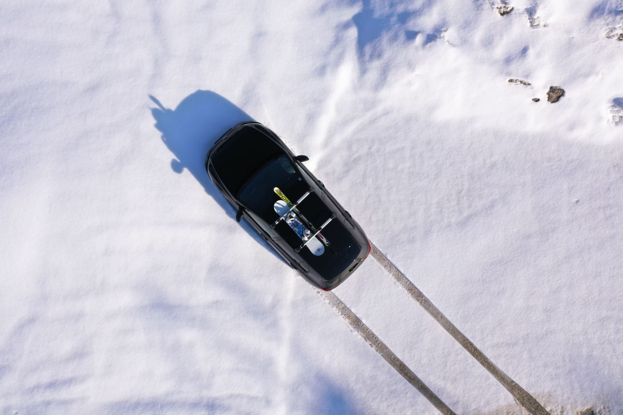 Black car with snowboard on roof driving through snow. Bird's eye perspective